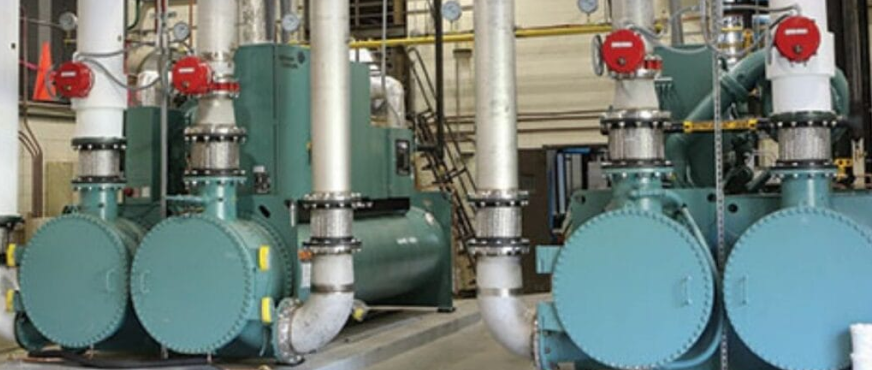 Industrial mechanical room with teal chiller compressor units and piping during professional chiller plant demolition services in New Jersey.