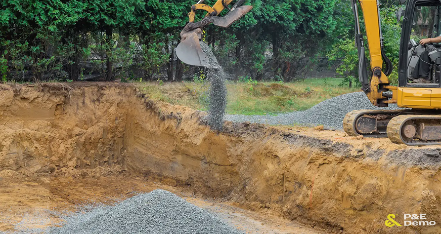 Excavator pouring gravel into excavation pit during professional concrete backfill services in New Jersey.