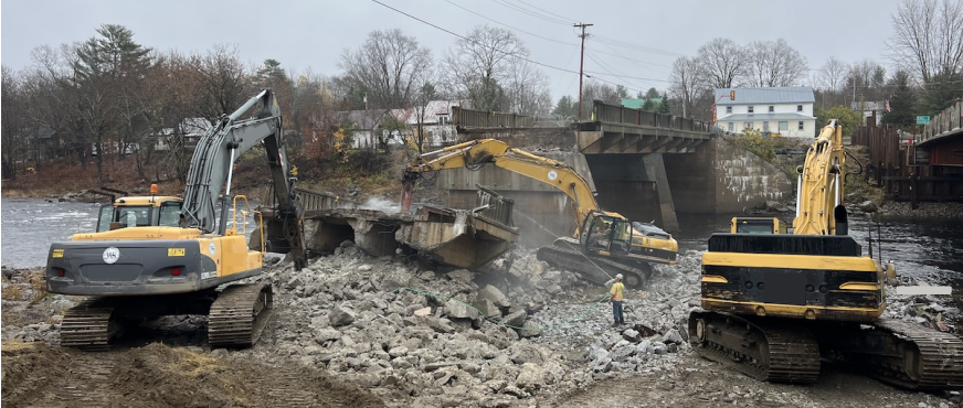 Three excavators demolishing concrete bridge over river during professional bridge demolition services in New Jersey.