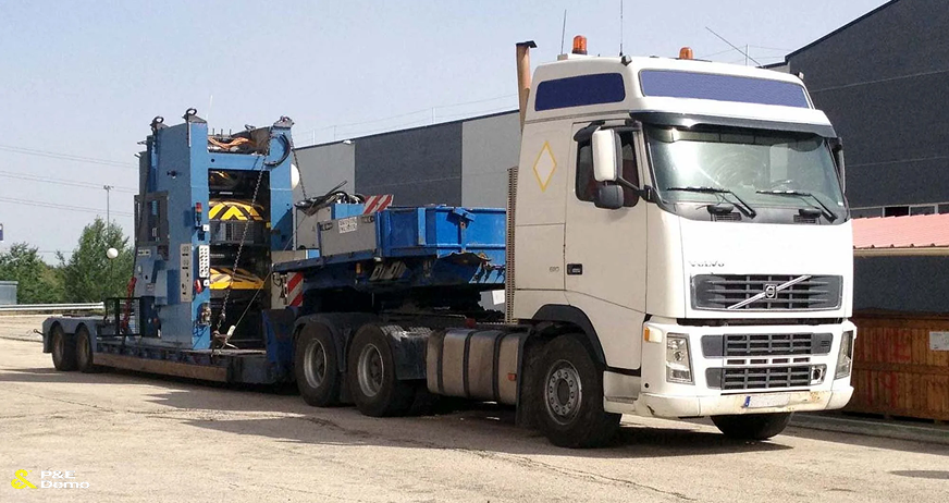 Flatbed truck transporting large industrial machine during professional heavy machinery removal services in New Jersey.