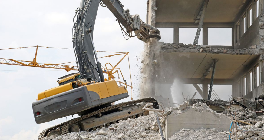 Excavator with hydraulic breaker demolishing multi‑story concrete building during professional mechanical demolition services in New Jersey.