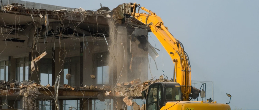 Excavator with hydraulic breaker demolishing upper section of multi‑story concrete office building during professional mechanical demolition services in New Jersey
