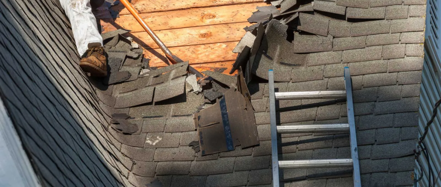 Worker removing asphalt shingles and exposing wooden roof decking during professional roof tear‑off services in New Jersey
