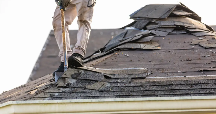 Worker removing asphalt shingles with a roofing shovel during professional roof tear‑off services in New Jersey