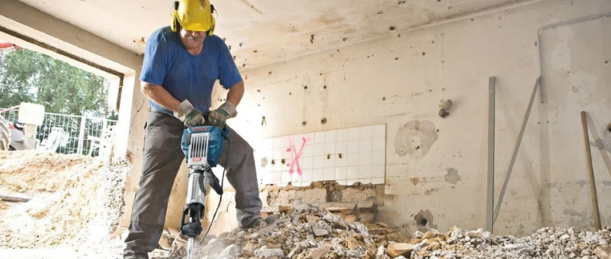 Construction worker using jackhammer to break rubble inside partially demolished building during professional selective demolition services in New Jersey.