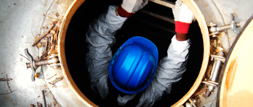 Worker in protective gear descending into a confined space via ladder during professional water tank removal in New Jersey