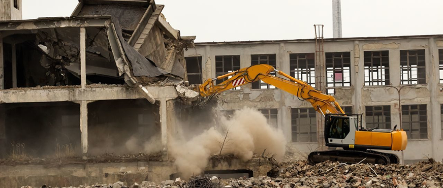 Excavator demolishing multi‑story concrete building with dust cloud during professional total demolition services in New Jersey.