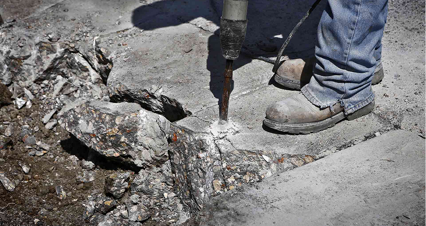 Worker using jackhammer to break concrete pavement during professional concrete removal services in New Jersey.