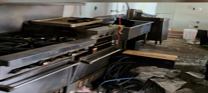 Abandoned commercial kitchen with industrial stove, deep sink, and cluttered floor during professional kitchen demolition services in New Jersey.