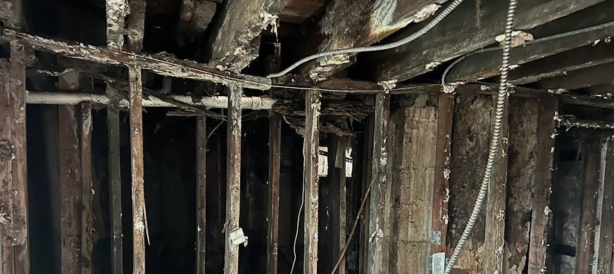 Damaged interior wall and ceiling with exposed studs, beams, and electrical wiring during professional full interior gut‑out demolition services in New Jersey.