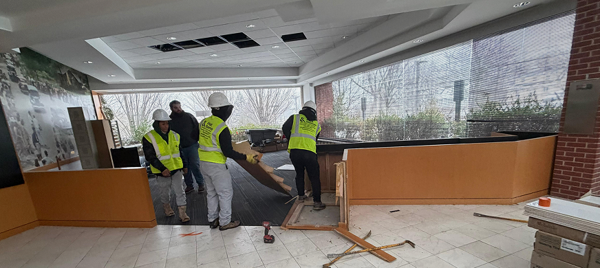 Construction workers dismantling wooden panels from reception desk during professional interior selective demolition services in New Jersey.