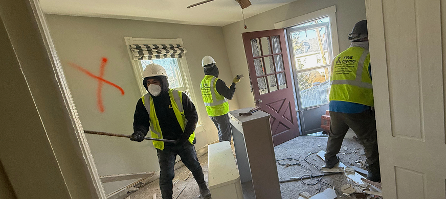 Three demolition contractors in safety gear removing interior brick wall using scaffolding during professional wall demolition services in New Jersey.