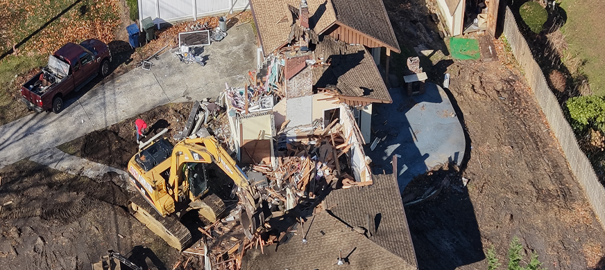 Excavator demolishing residential house with debris scattered during professional structural demolition services in New Jersey.